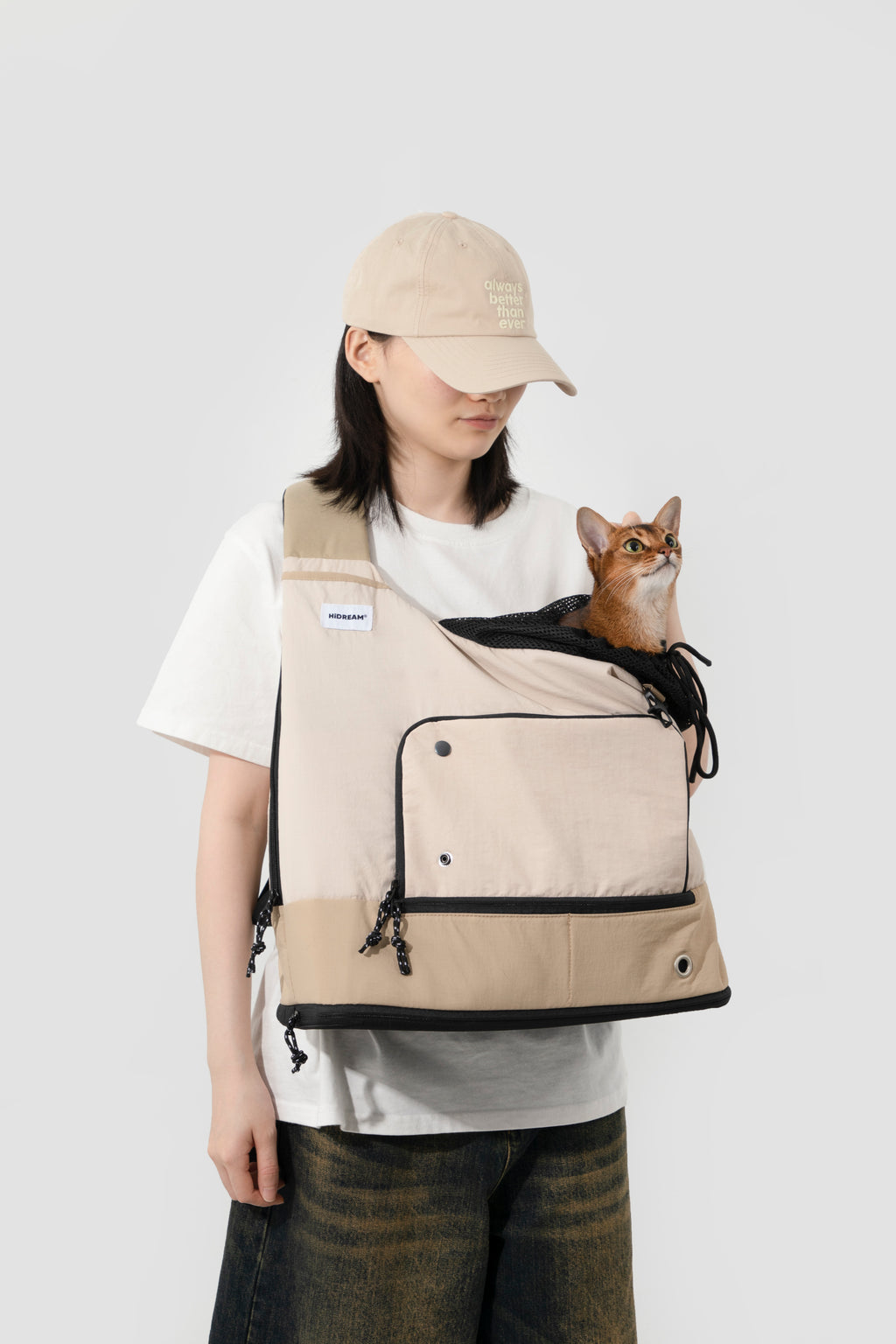 Woman carrying a cat in beige HiDREAM Crossbody Travel Bag for Pets, breathable mesh top and secure drawstring closure visible.