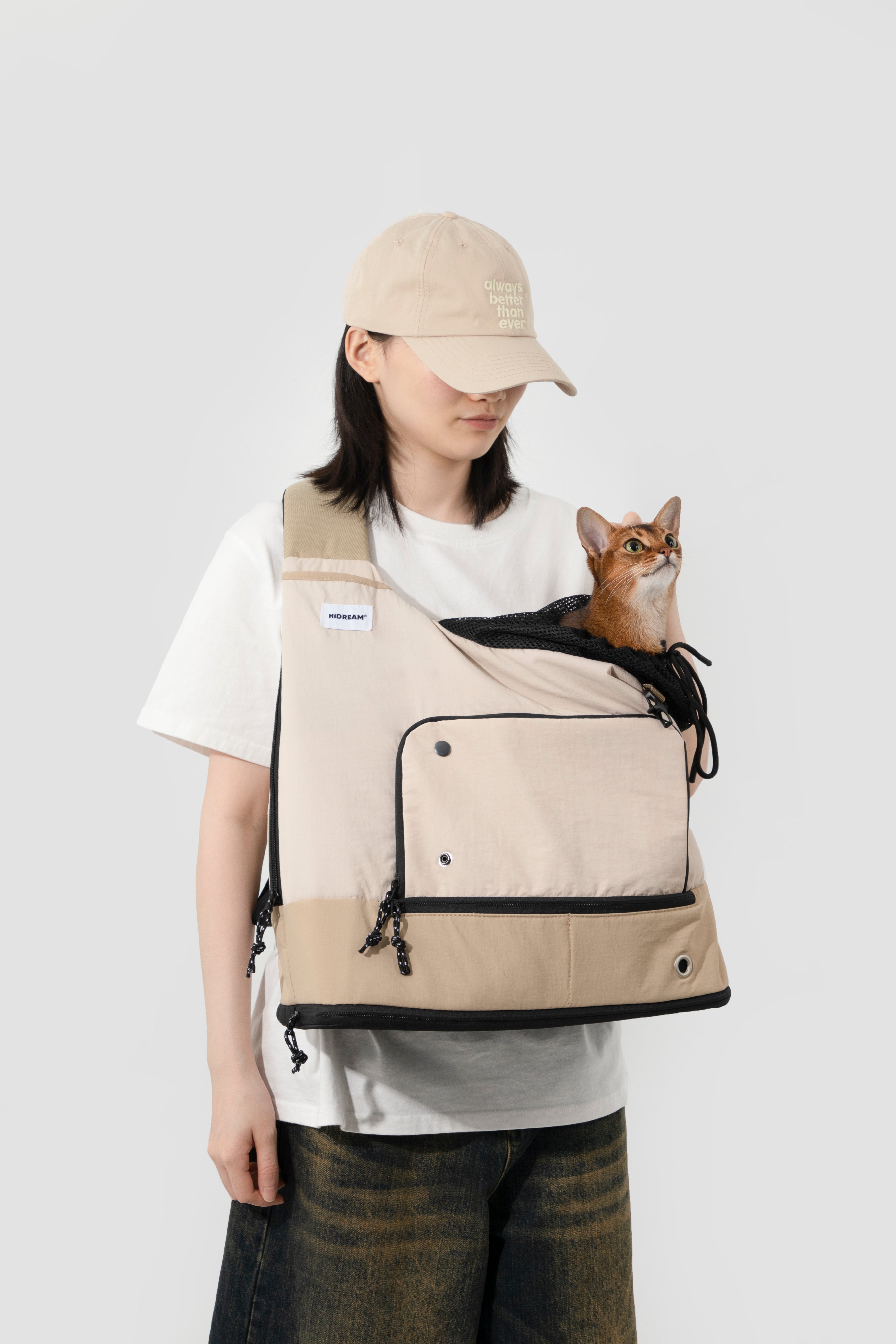 Woman carrying a cat in beige HiDREAM Crossbody Travel Bag for Pets, breathable mesh top and secure drawstring closure visible.