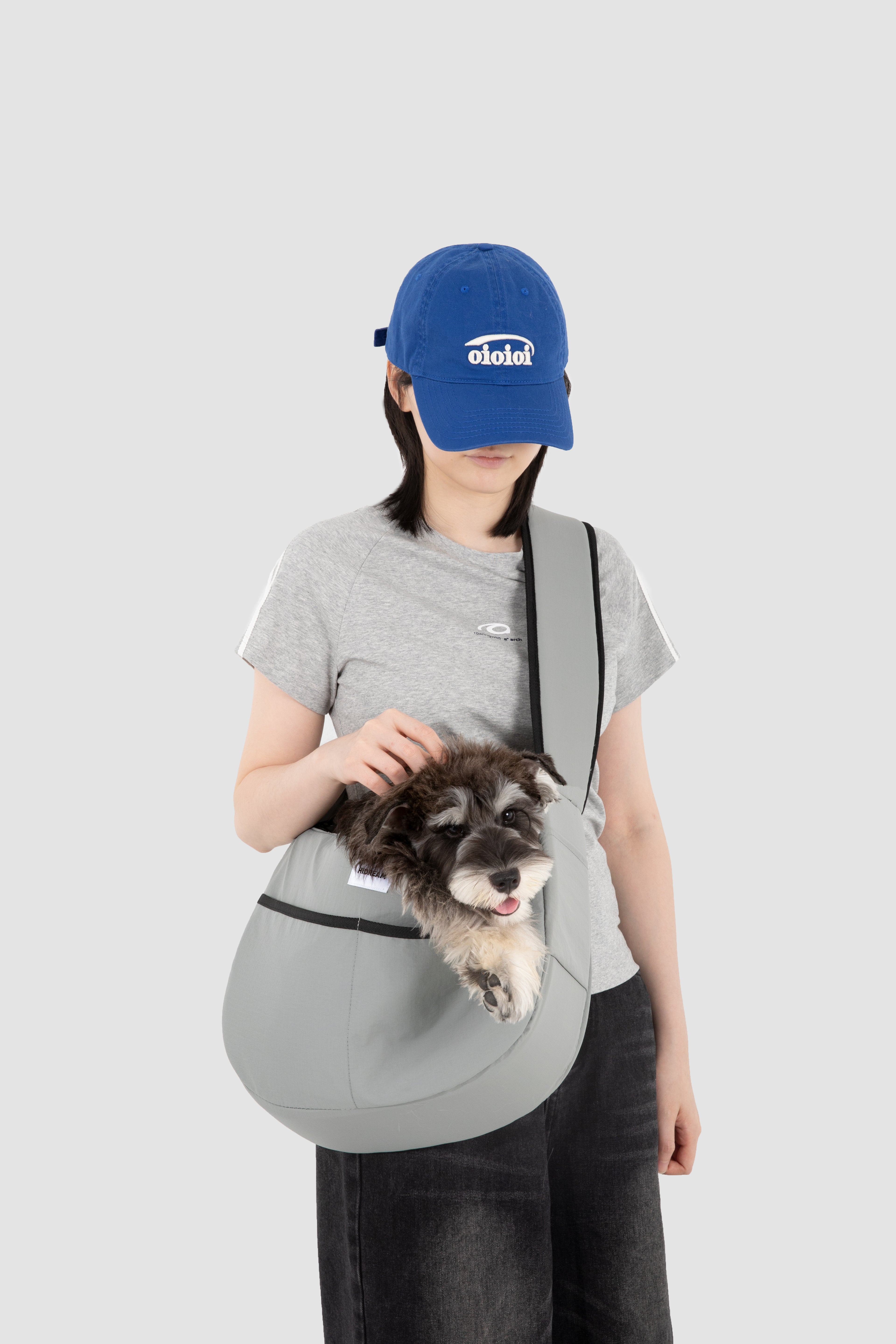 Small dog peeking out of grey HiDREAM Crossbody Pet Carrier Tote worn by a woman. Ergonomic and escape-proof for safe pet outings.