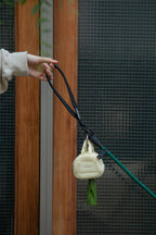 Yellow HiDREAM Dog Poop Bag Holder clipped to leash, dispensing waste bags during a walk near wooden gate.