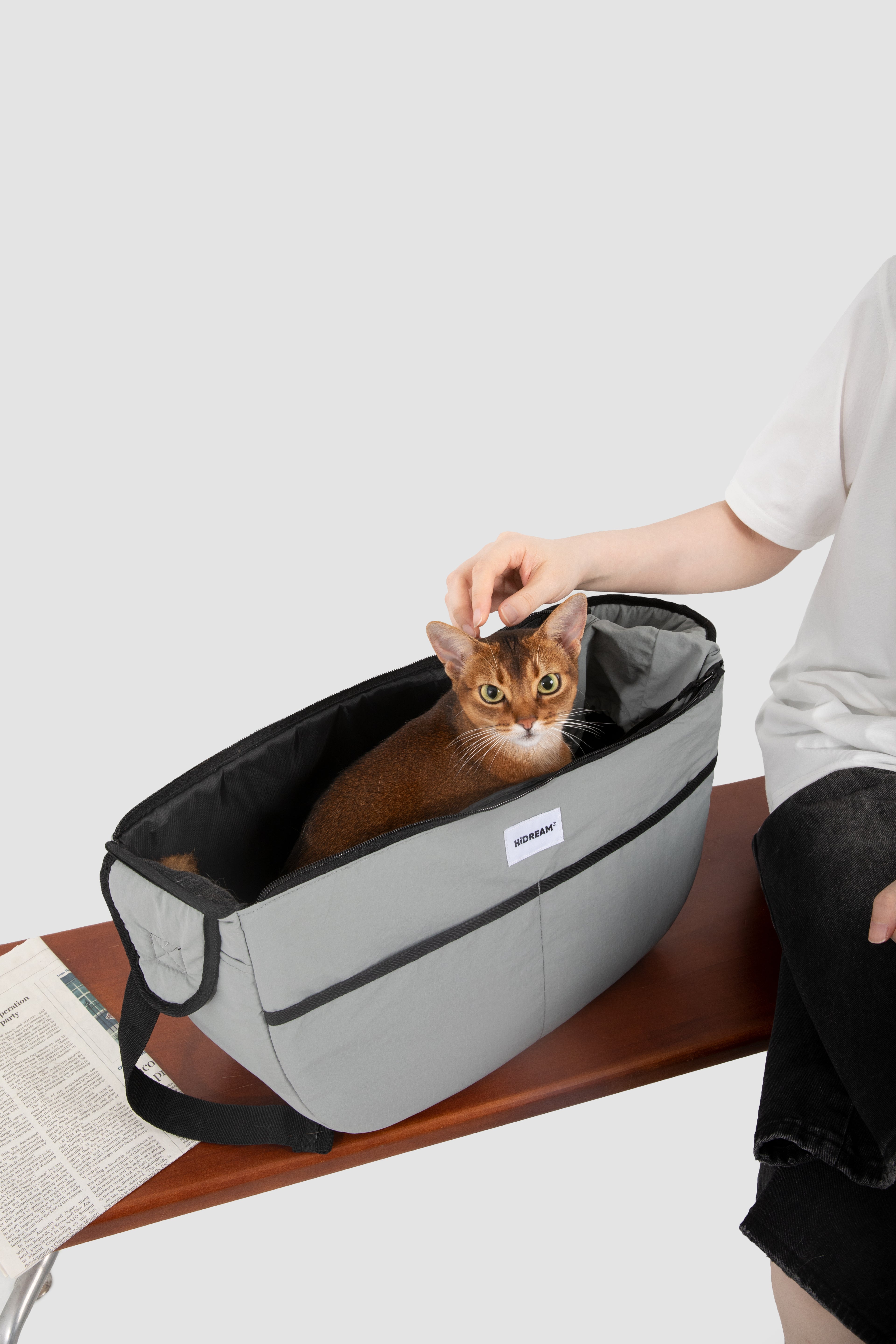 Brown cat sitting in grey HiDREAM Crossbody Pet Carrier Tote on a bench. Lightweight and cozy for indoor or outdoor pet use.