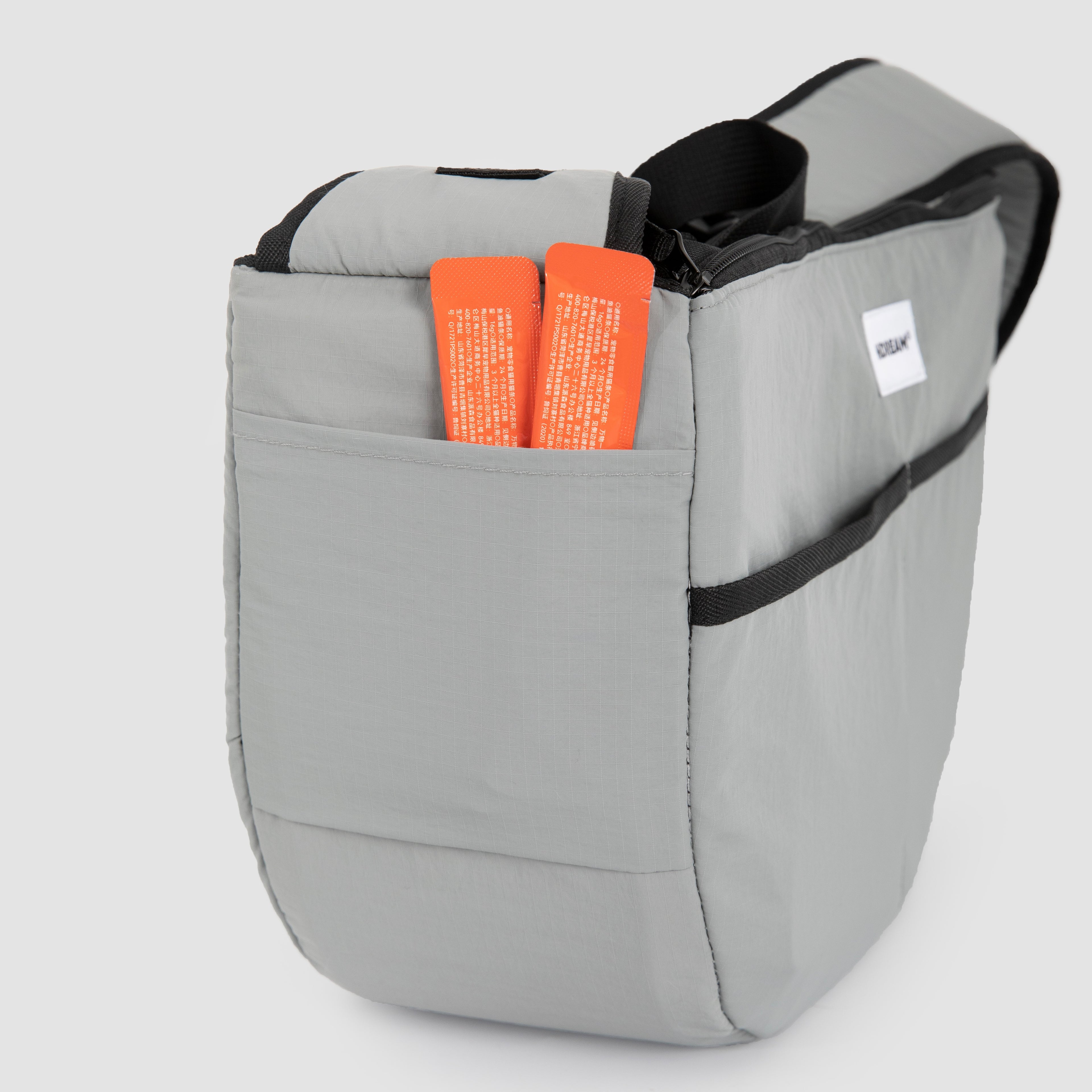 Side pocket of grey HiDREAM Crossbody Pet Carrier Tote holding pet accessories. Extra storage for treats, leashes, or documents.